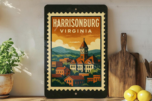 A framed vintage postage stamp depicting a cityscape of Harrisonburg, Virginia, with a clock tower and buildings, is displayed on a shelf next to a wooden cutting board and a potted plant.