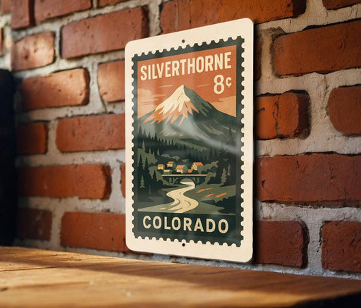 A metal sign with a mountain landscape and a river, mounted on a brick wall.