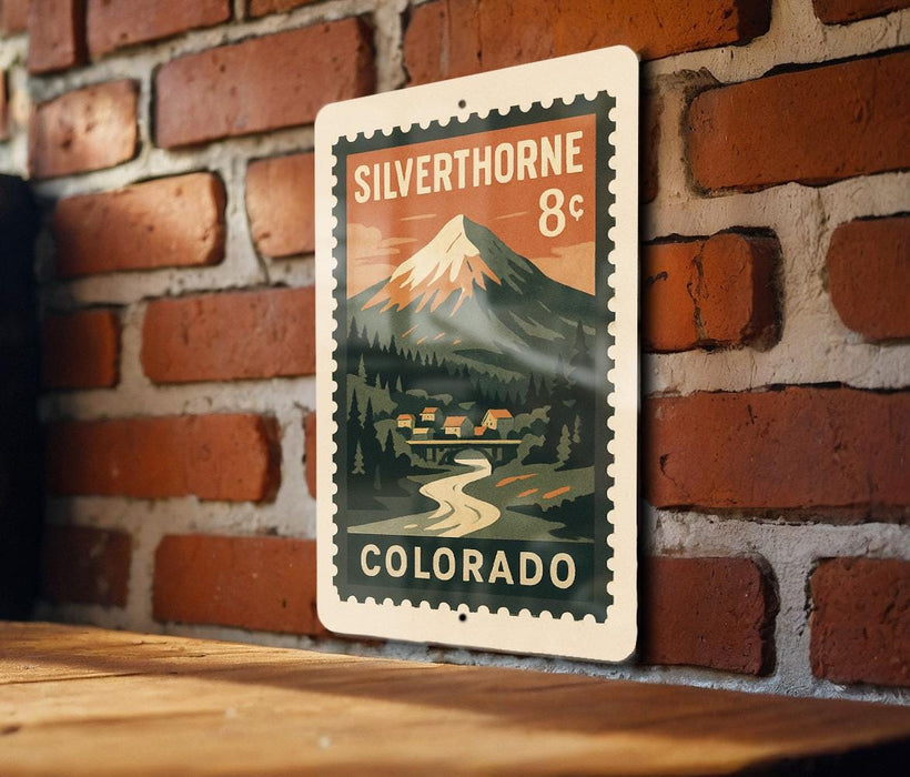 A metal sign with a mountain landscape and a river, mounted on a brick wall.