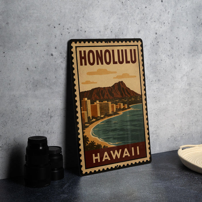 A vintage-style metal sign with the text "HONOLULU" and "HAWAII" printed on it, depicting a beach scene with mountains in the background.