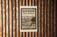 A U.S. postage stamp from California, featuring a street scene and mountains, is displayed on a wooden wall.