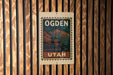 A vintage-style sign with the word "OGDEN" and "UTAH" printed on it, mounted on a wooden wall.