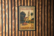 A vintage postage stamp from California featuring a car and a bell tower, mounted on a wooden wall.