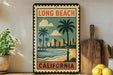 A vintage-style metal sign with a tropical beach scene and palm trees, featuring the text "LONG BEACH CALIFORNIA" in the center.