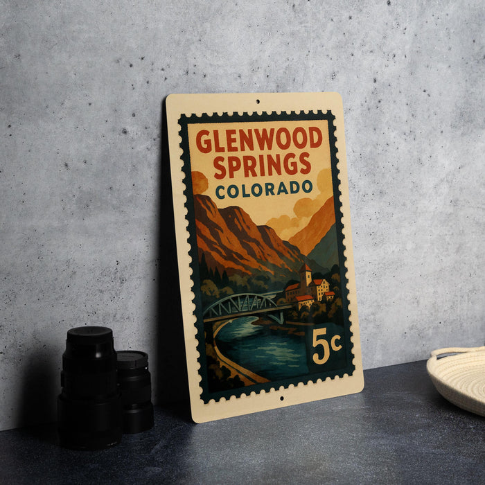 A vintage Glenwood Springs, Colorado postage stamp is displayed on a table, featuring a scenic mountain landscape and a bridge.