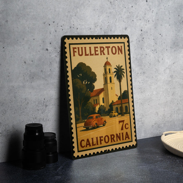 A vintage postage stamp from Fullerton, California, featuring a car and a bell tower, placed on a countertop next to some black camera lenses.