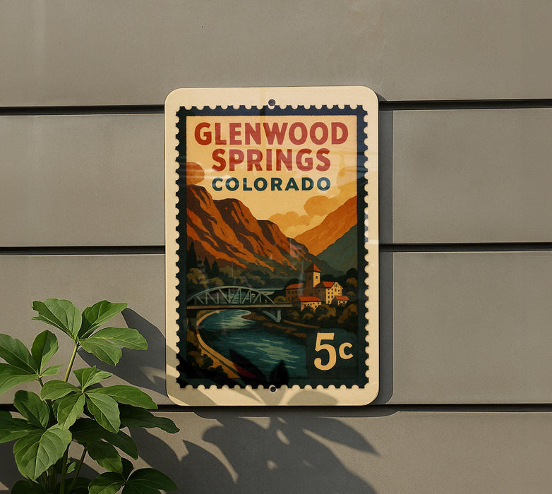 A postage stamp-like sign for Glenwood Springs, Colorado, featuring a scenic mountain landscape with a bridge and river.