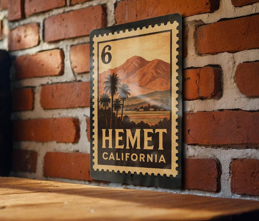 A metal sign with a vintage-style illustration of a tropical landscape, featuring palm trees and mountains, mounted on a brick wall.