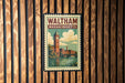 A vintage-style poster of Waltham, Massachusetts, featuring a clock tower and a river, is displayed on a wooden wall.