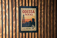 A vintage-style postage stamp from Odessa, Texas, featuring a silhouette of the city skyline and a tower, mounted on a wooden wall.