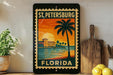A framed vintage-style stamp depicting St. Petersburg, Florida, with a palm tree and sunset in the background.