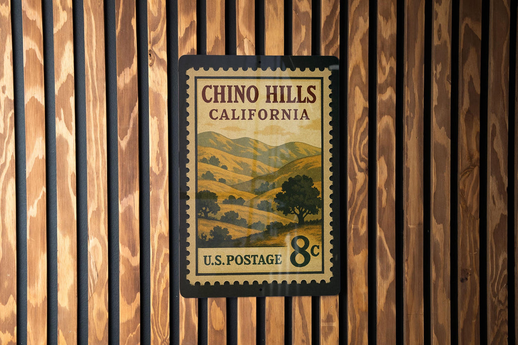 A vintage postage stamp from California, featuring a scenic landscape with hills and trees, mounted on a wooden wall.