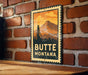 A metal sign with the text "BUTTE MONTANA" and an illustration of a mountain and a tower, mounted on a brick wall.