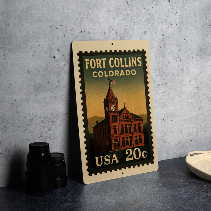 A metal sign with a vintage-style illustration of a building and a clock, featuring the text "Fort Collins, Colorado" and "USA 20c" printed on it.