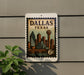 A postage stamp-like sign displaying the city of Dallas, Texas, with a skyline and a bridge.