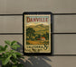 A vintage-style postage stamp from California, featuring a rural landscape and a house, is displayed on a wall.