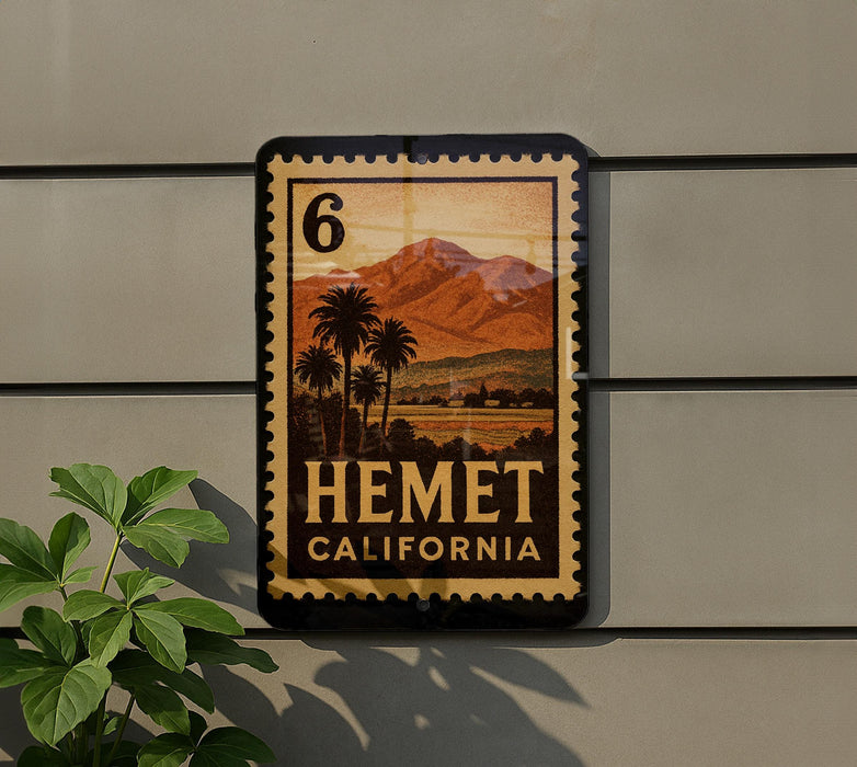 A vintage-style metal sign with a palm tree and mountains, mounted on a wall, with a plant to the left.