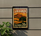 A vintage-style postage stamp from San Ramon, California, featuring a landscape with mountains and a tree, mounted on a wall.