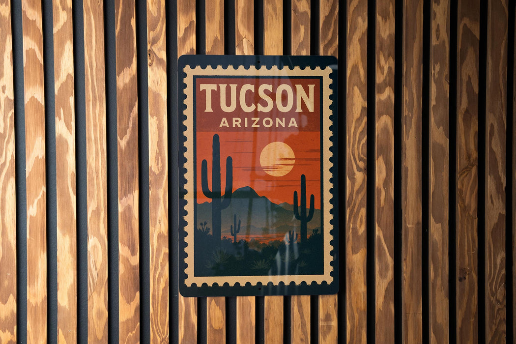 A vintage-style postage stamp depicting the city of Tucson, Arizona, with a cactus landscape and a sunset in the background.