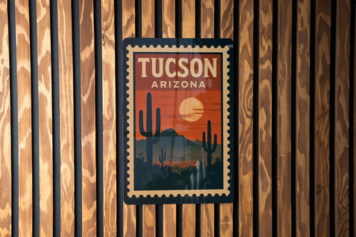A vintage-style postage stamp depicting the city of Tucson, Arizona, with a cactus landscape and a sunset in the background.