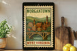 A framed vintage-style poster of Morgantown, West Virginia, featuring a cityscape with a bridge and mountains in the background.