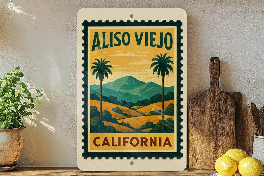 a vintage-style sign for Aliso Viejo, California, with a palm tree and landscape illustration. The sign is displayed on a shelf next to a wooden cutting board and a potted plant.