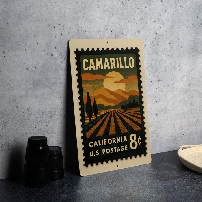 A vintage postage stamp from California, featuring a landscape with mountains, trees, and a sunset, placed on a countertop next to some black camera lenses.