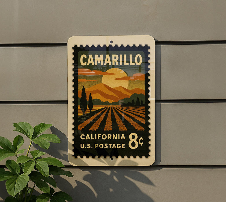 A postage stamp-like sign with a scenic landscape of mountains, fields, and a sunset, mounted on a wall.