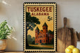 A framed vintage postage stamp from Tuskegee, Alabama, depicting a brick building with a green roof, placed on a wooden shelf next to a wooden cutting board and a potted plant.