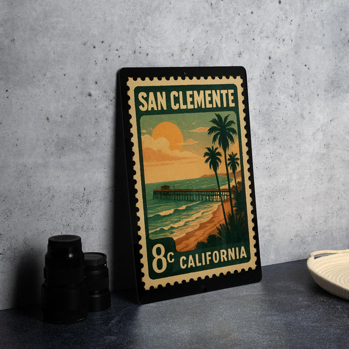 A framed postcard with a beach scene and palm trees, featuring a sunset and a pier, is displayed on a table.
