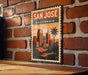 A vintage-style metal sign with the text "SAN JOSE CALIFORNIA" and an illustration of a city skyline with palm trees.