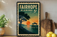 a vintage-style metal sign with a sunset scene, including a pier and a tree, displayed on a shelf next to a wooden cutting board and a potted plant.