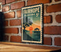 A vintage-style metal sign with the text "FAIRHOPE ALABAMA 5c" and an illustration of a sunset over a body of water with a pier and a tree.