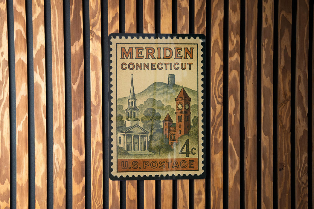 A vintage U.S. postage stamp from Connecticut, featuring a church and a clock tower, is displayed on a wooden wall.