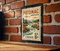A vintage-style metal postage stamp depicting a scenic landscape with a river and mountains, mounted on a brick wall.
