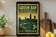 A vintage postage stamp from Wisconsin, featuring a cityscape and a river, is displayed on a shelf next to a wooden cutting board and a potted plant.