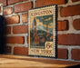 A vintage-style postage stamp from the United States, featuring a town scene with a clock tower, mounted on a brick wall.