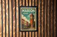 A vintage postage stamp from Marion, Iowa, featuring a clock tower and buildings, is displayed on a wooden wall.