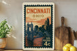 A vintage-style postage stamp from the United States, featuring the cityscape of Cincinnati, Ohio, with a bridge and buildings in the background.