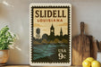 A vintage-style postage stamp from Louisiana, featuring a silhouette of a city skyline with a clock tower, displayed on a shelf next to a wooden cutting board and a potted plant.