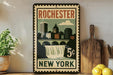 A vintage-style poster of Rochester, New York, featuring a cityscape with a waterfall, displayed on a wall next to a wooden cutting board and some lemons.