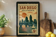 A framed vintage-style poster of San Diego, California, featuring a cityscape with a bridge and sailboat, is displayed on a wall next to kitchen utensils and a potted plant.