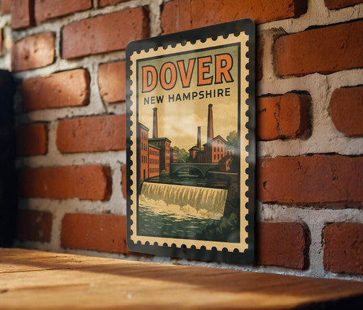 A vintage-style poster of Dover, New Hampshire, featuring a brick wall and a waterfall, is displayed on a wooden surface.