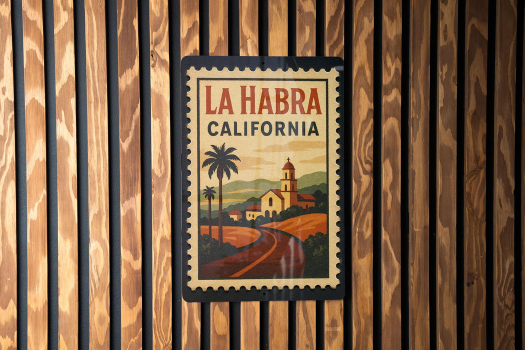 A framed poster of La Habra, California, featuring a palm tree and a road leading to a church, is displayed on a wooden wall.
