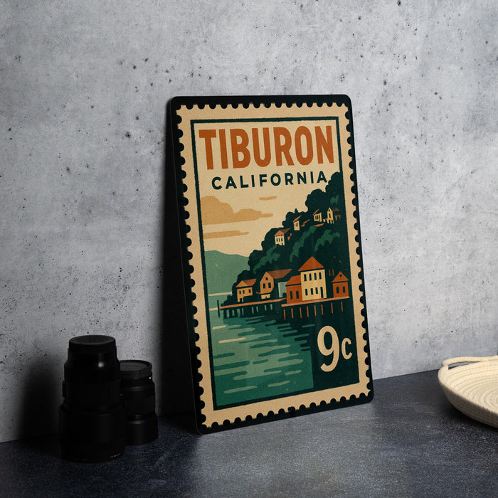 A vintage postage stamp from California, featuring a coastal town scene, is displayed on a table next to some black camera lenses.