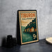 A vintage postage stamp from California, featuring a coastal town scene, is displayed on a table next to some black camera lenses.