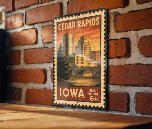 A vintage-style postage stamp from Iowa featuring a cityscape with a bridge and trees, mounted on a brick wall.