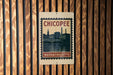 A metal sign with the text "CHICOPEE" and "MASSACHUSETTS" printed on it, mounted on a wooden wall.