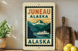 a vintage-style sign for Juneau, Alaska, with a mountain landscape and a boat on the water.