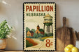 A vintage-style metal sign for Papillion, Nebraska, featuring a water tower and a small town landscape.